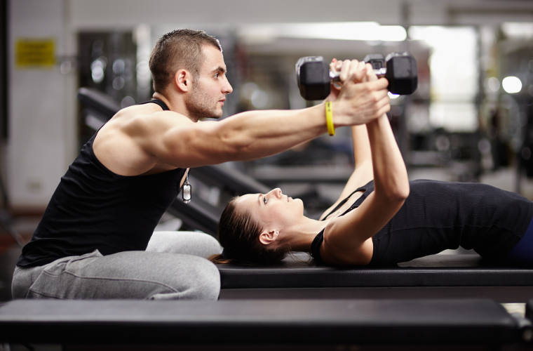 Personal trainer helping woman working with heavy dumbbells